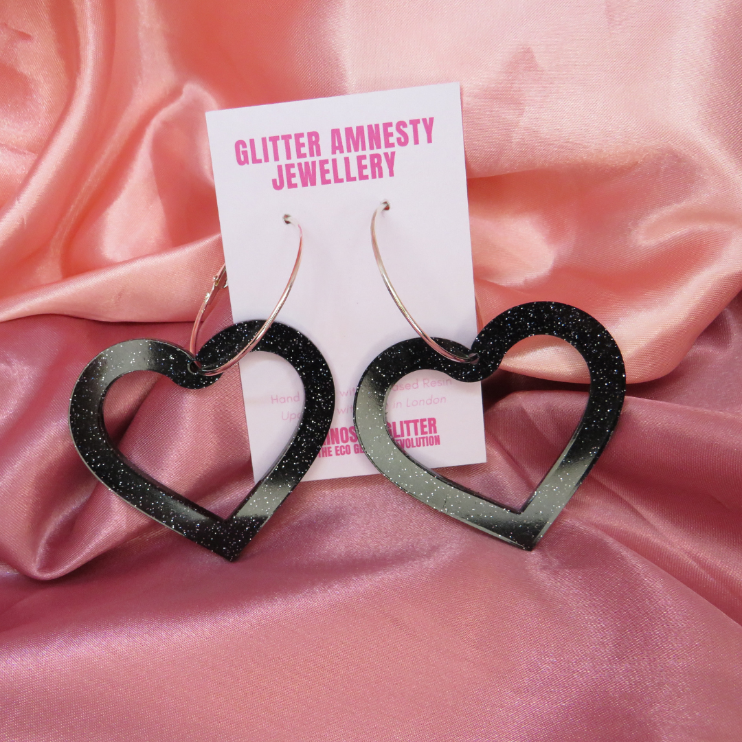 Giant black love heart glitter earrings by Luminosity Glitter on a silky pink background