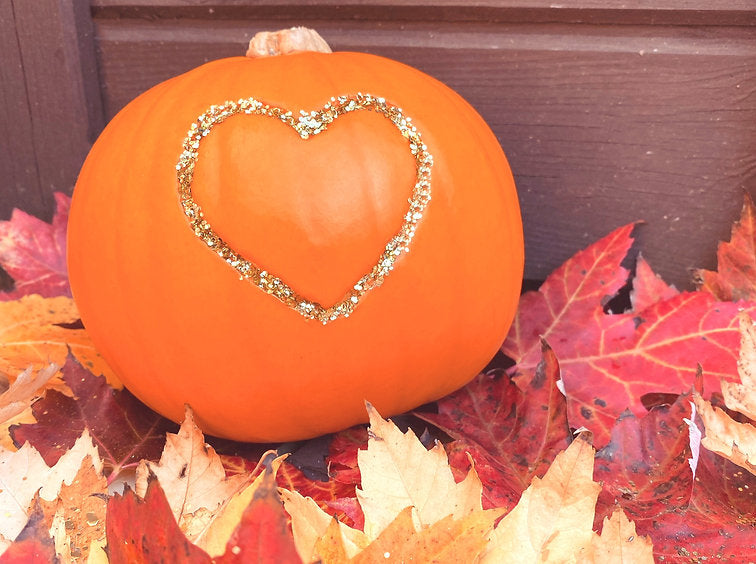 A baby pumpkin on autumn leaves with a gold glitter heart