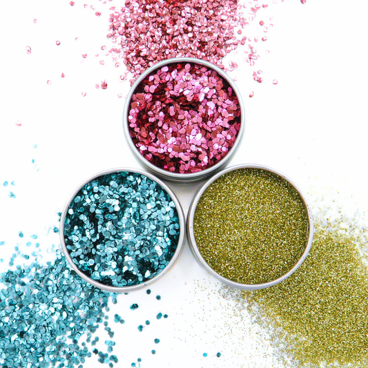 Three small bowls filled with pink, blue, and gold glitter on a white background.