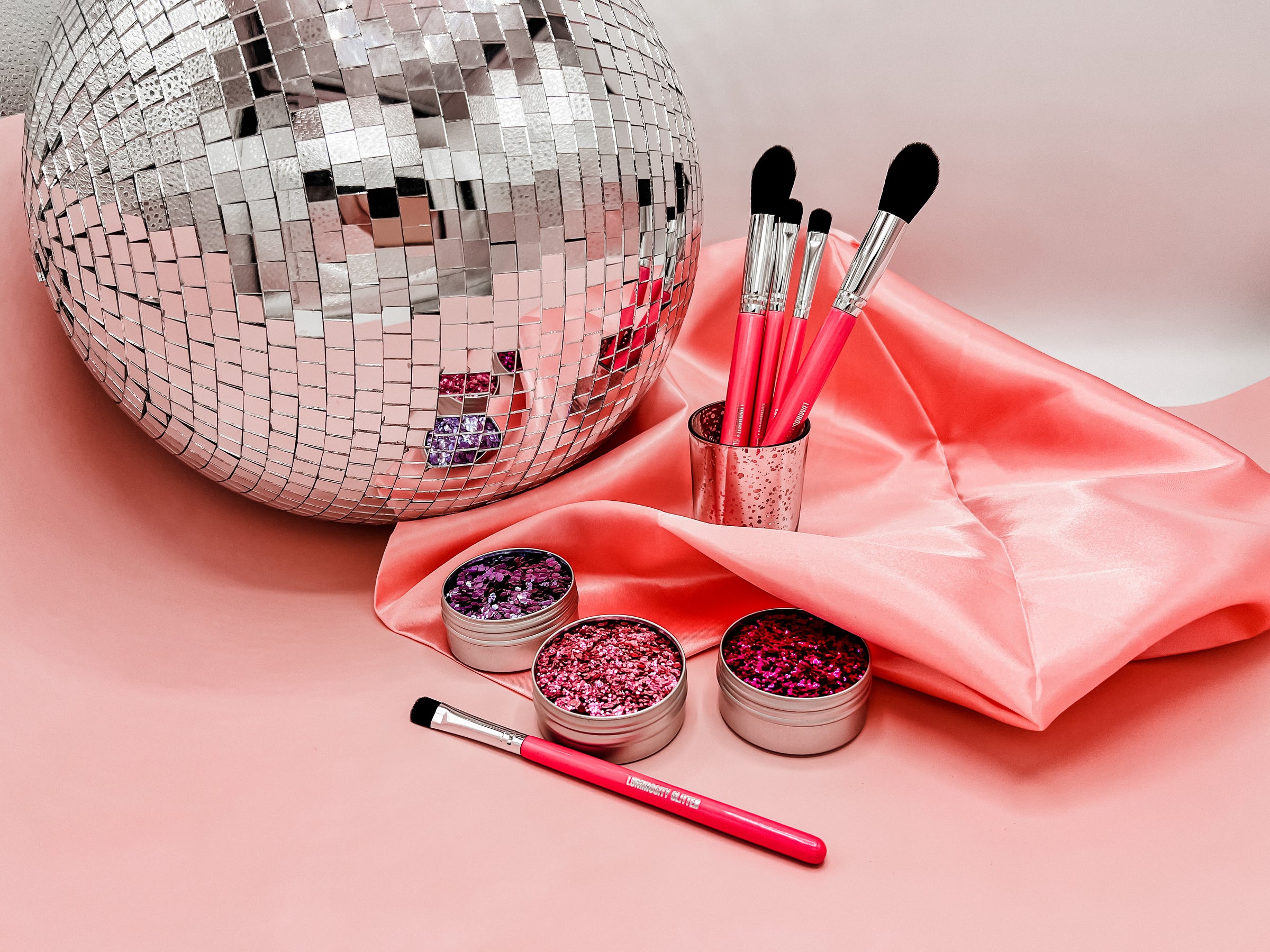 Giant disco ball with eco friendly glitter and hot pink makeup brushes on a pink and silk pink background