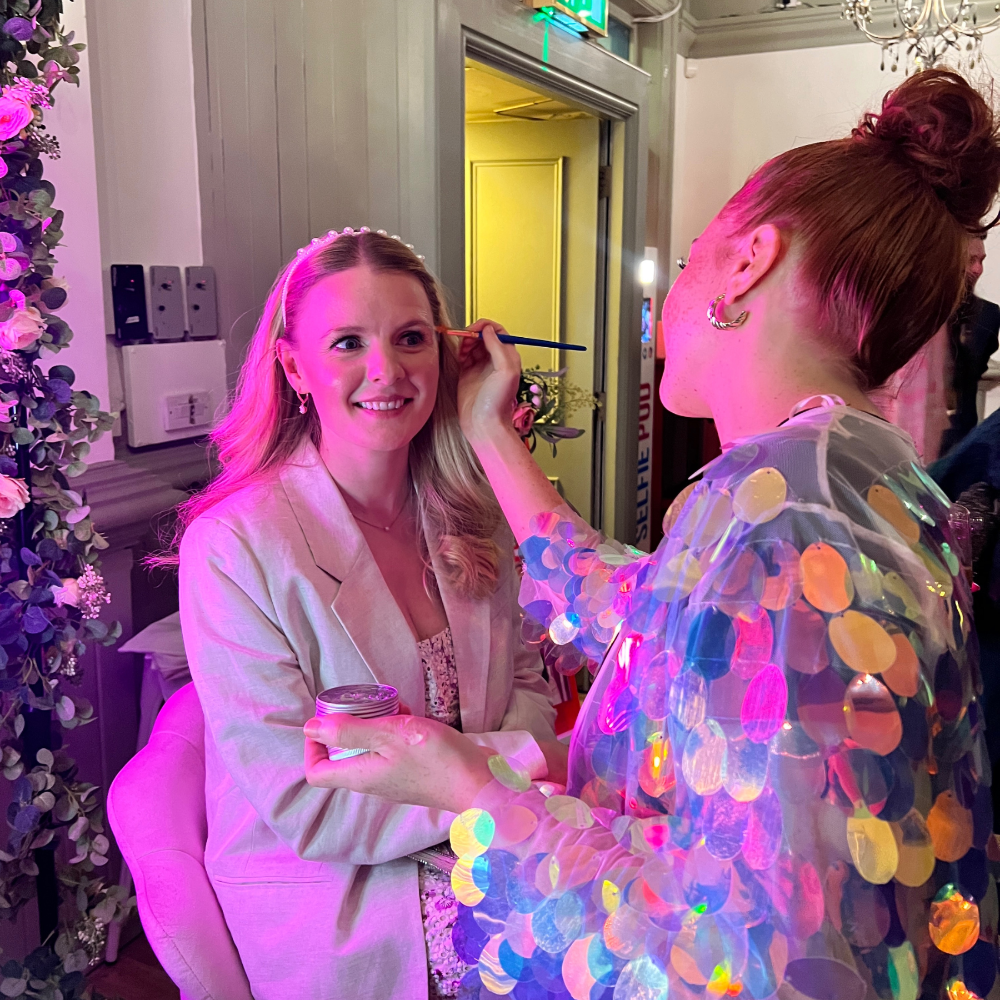 An eco glitter artist wearing a sequin jacket, glittering a guests face at a wedding in London