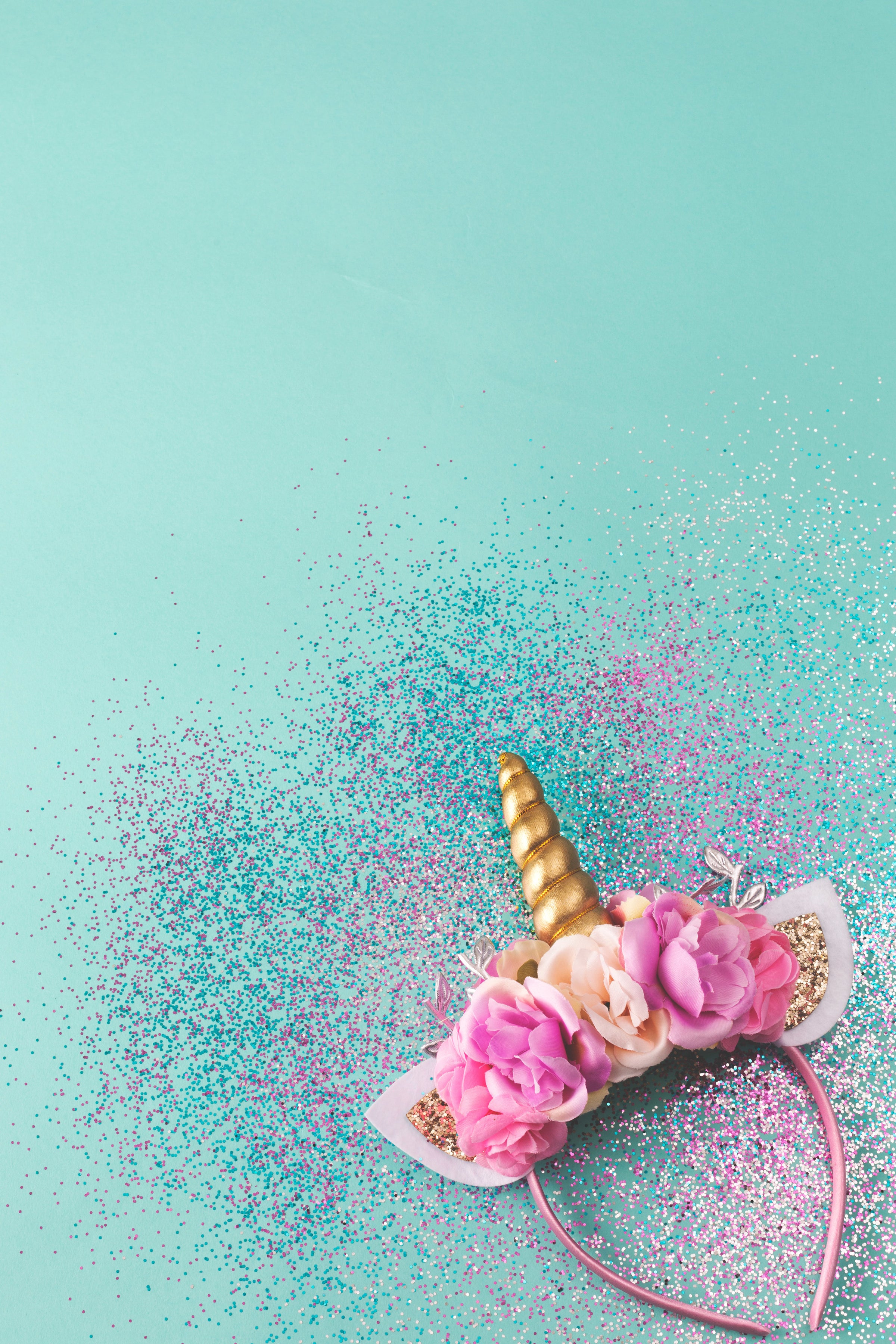 Turquoise background with glitter sprinkled over it and a unicorn headband