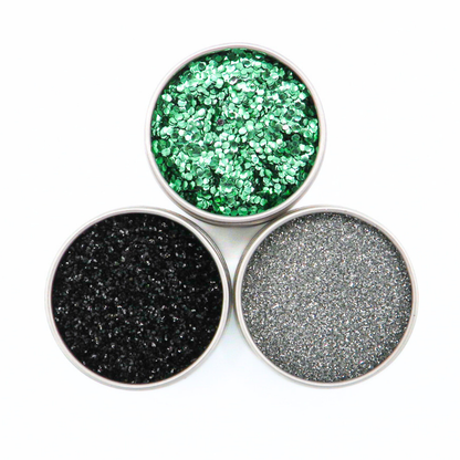 Three round containers of glitter in green, black, and gray on a white background