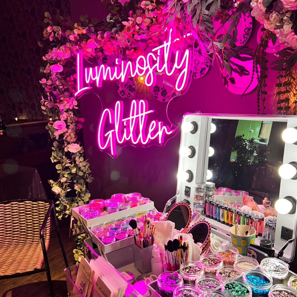 Luxury eco glitter bar hire in london, surrey, berkshire and surrounding areas. Luminosity Glitter's luxury light up pop up hollywood mirror glitter bar with a hot pink neon sign and foral garland.