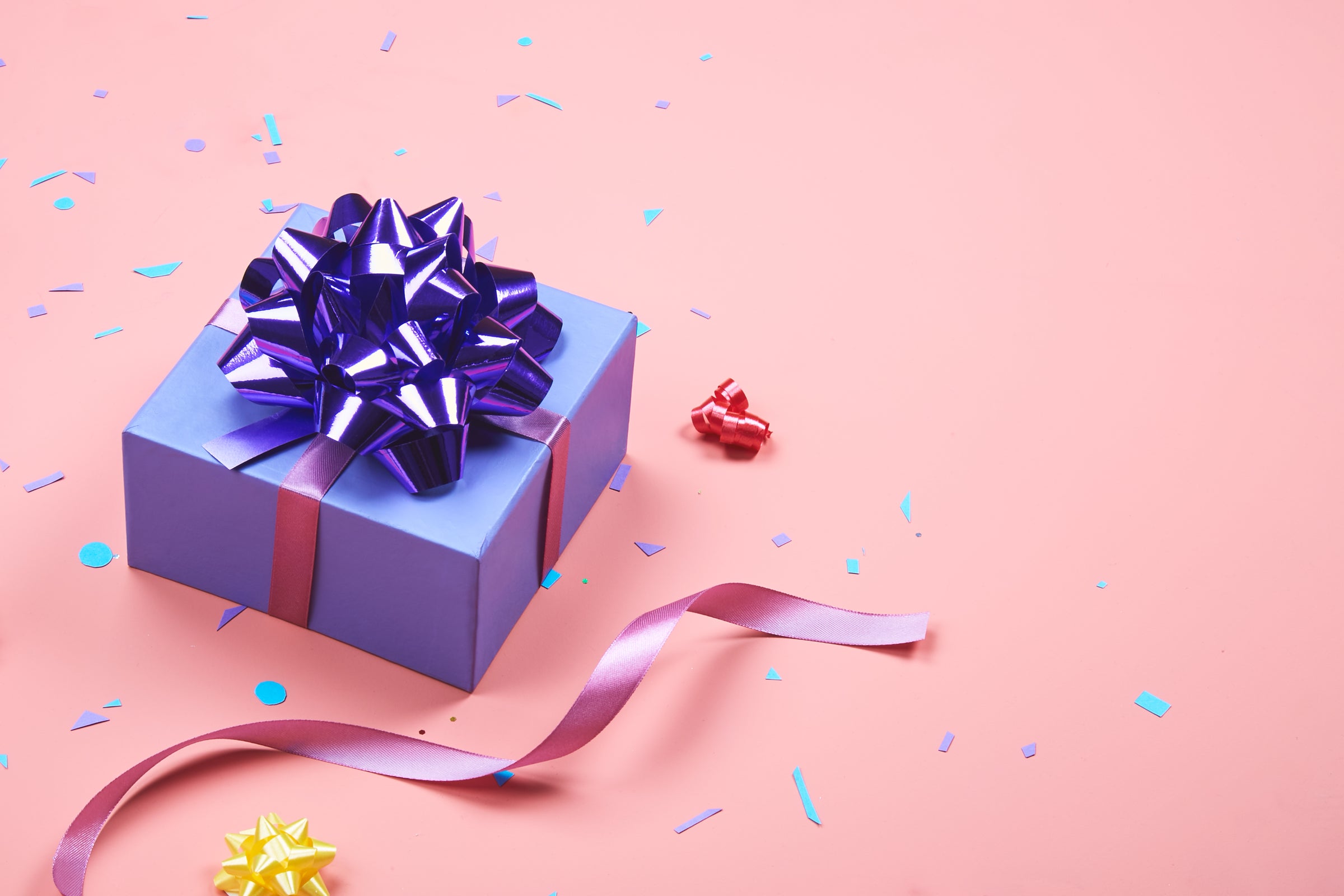 Purple gift wrapped with purple ribbon and on a pink background