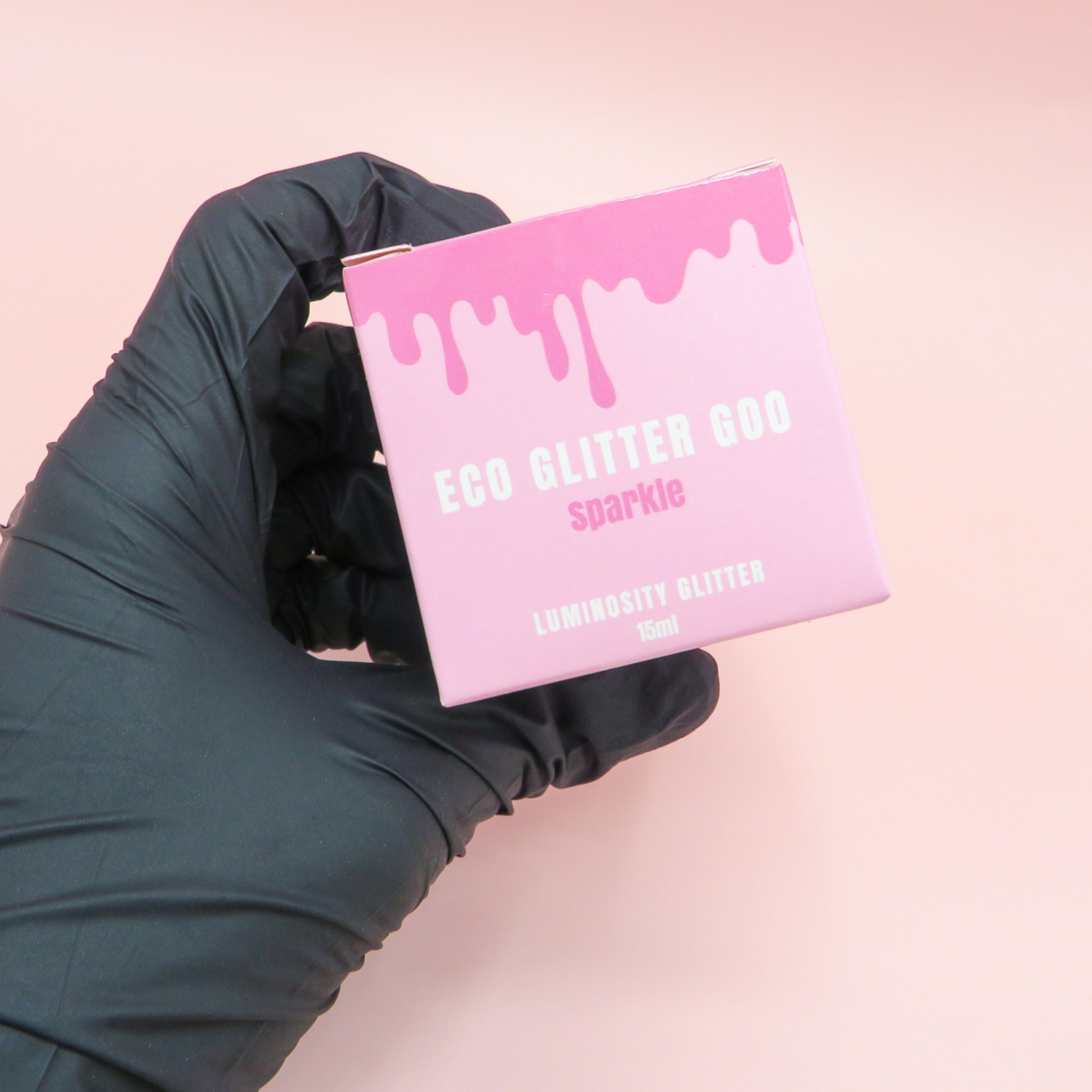 Black glove holding Luminosity Glitter's Eco Glitter Goo pink packaging for their glitter body gel