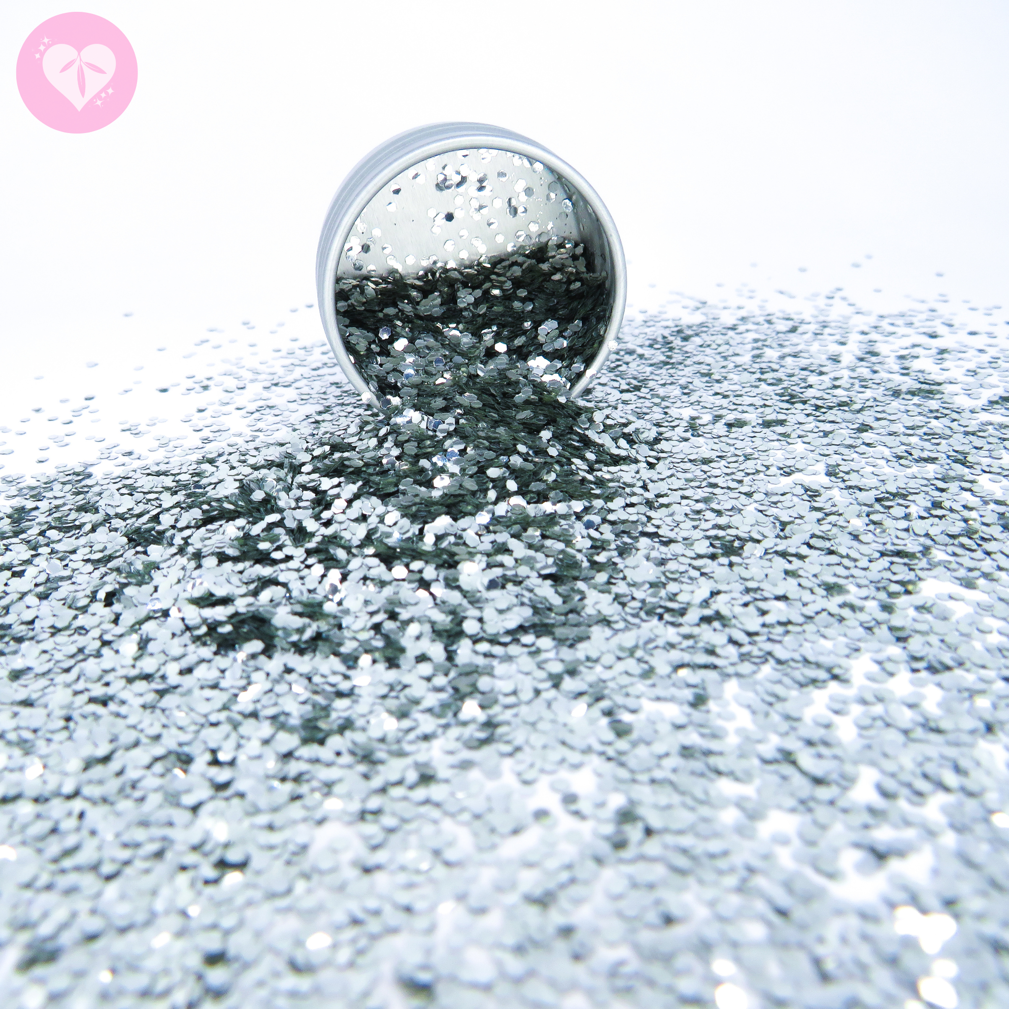 Silver chunky biodegradable glitter spilling from an aluminium pot onto a white surface