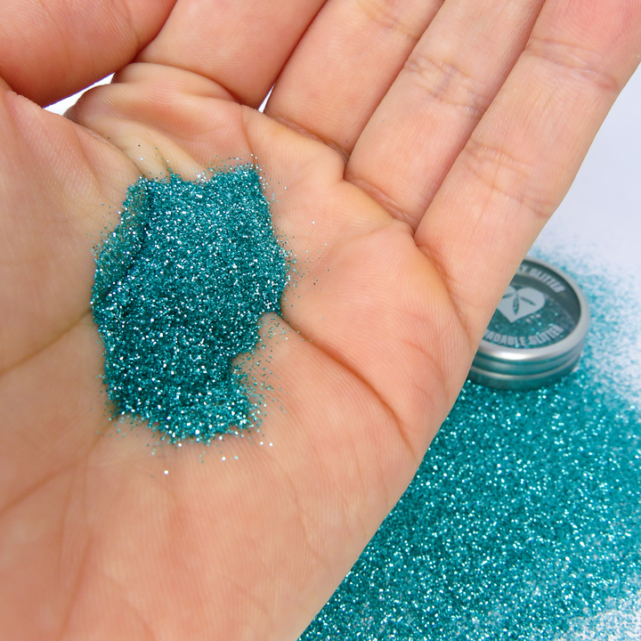Turquoise fine eco friendly cosmetic glitter by Luminosity Glitter. A scoop of turquoise glitter being held in a Caucasian hand.